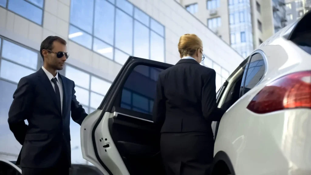 A chauffeur dressed in formal attire opening the door of a sleek black limousine to welcome a passenger.