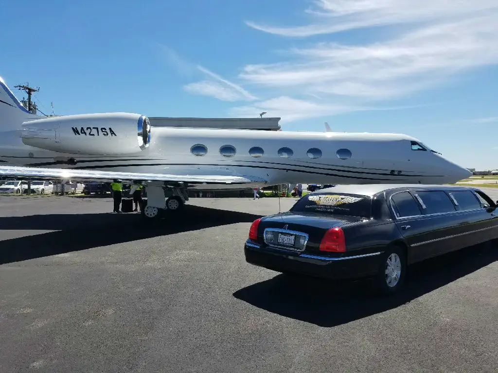 A luxury Professional airport limo is parked with a white private jet and maintenance crew on standby for delivering the burlington limo service