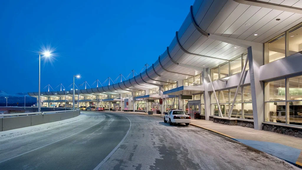 A modern airport terminal for oakville airport limo service illuminated at twilight, featuring a curved design, large glass windows, and a snowy pathway for arriving vehicles.