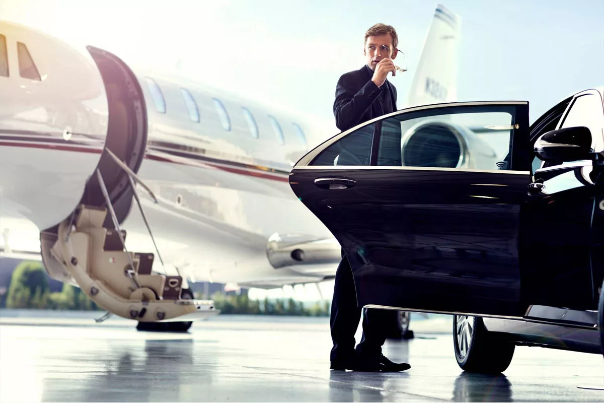 A chauffeur of oakville limo service is standing with a black limo while a private jet is parked at the bacjground