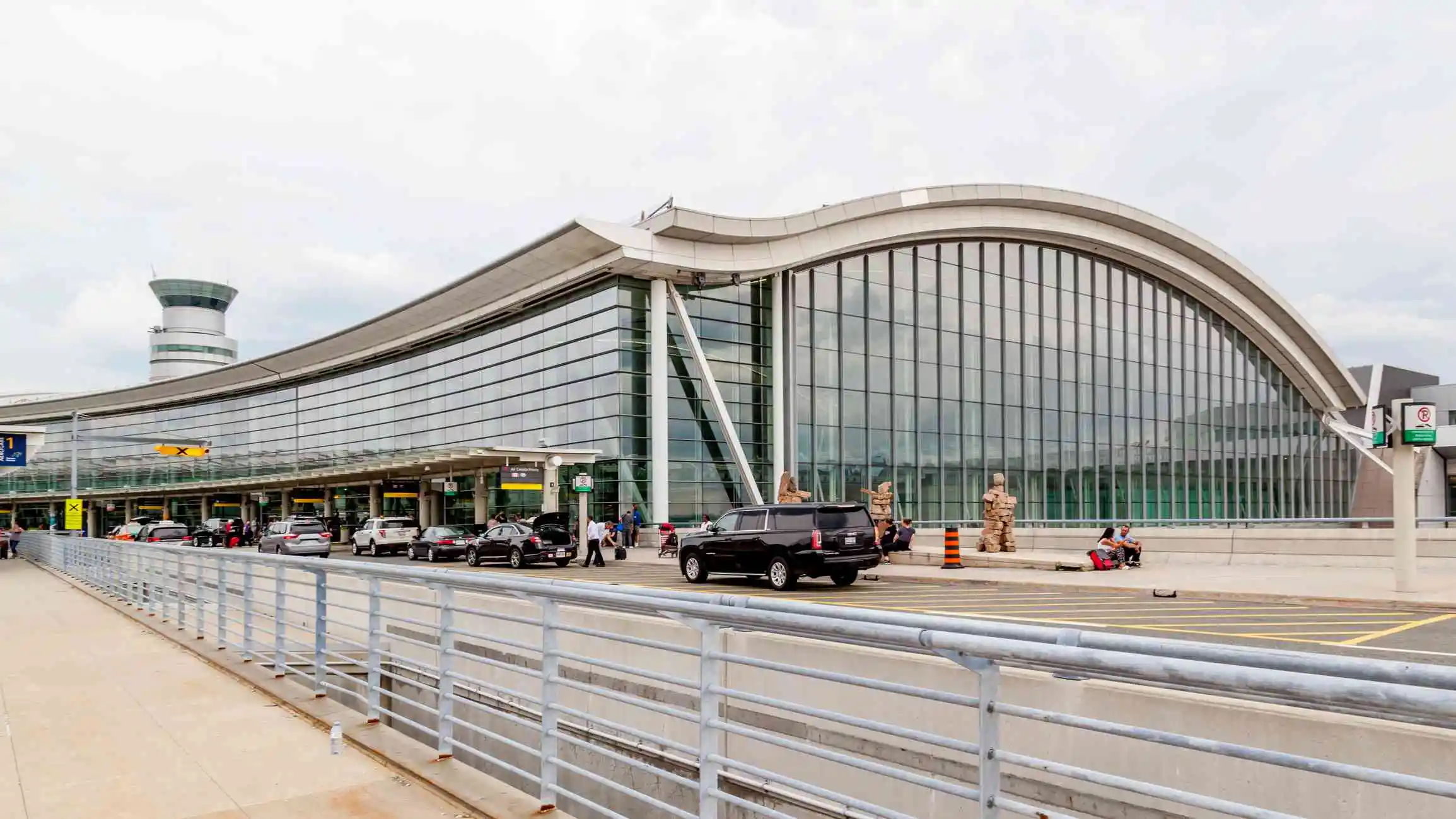 kitchener airport limo services-Modern airport exterior with large glass windows, vehicles parked in front, and a control tower in the background.