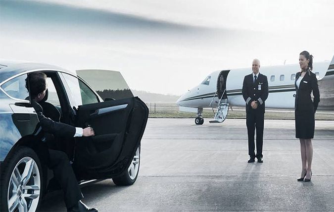 cambridge airport limo-A luxury car parked near a private jet on an airport tarmac, with a man stepping out of the car and two uniformed flight crew members standing nearby, ready to welcome him.