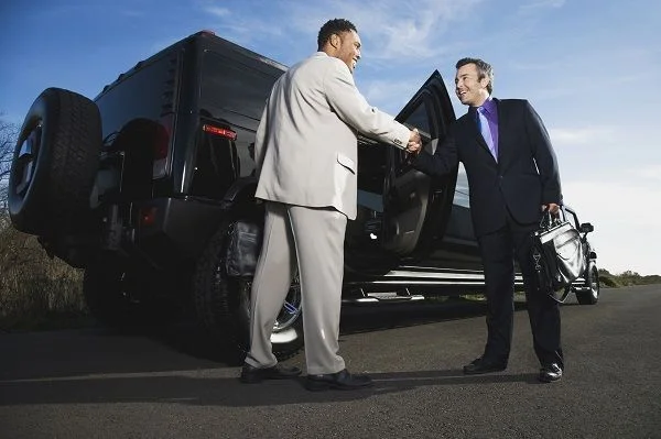 niagara falls limo service-Two men in suits shake hands on a road beside a large black SUV, suggesting a successful business meeting. The sky is clear, creating a professional and upbeat tone.