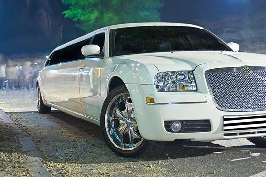 burlington airport limo service-A sleek white limousine parked under dim lights, showcasing shiny chrome wheels and a luxurious, elongated design.