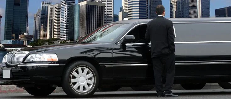 family friendly limo-A well-dressed man stands beside a sleek black limousine on a city street, with tall skyscrapers in the background, creating a luxurious and professional atmosphere.