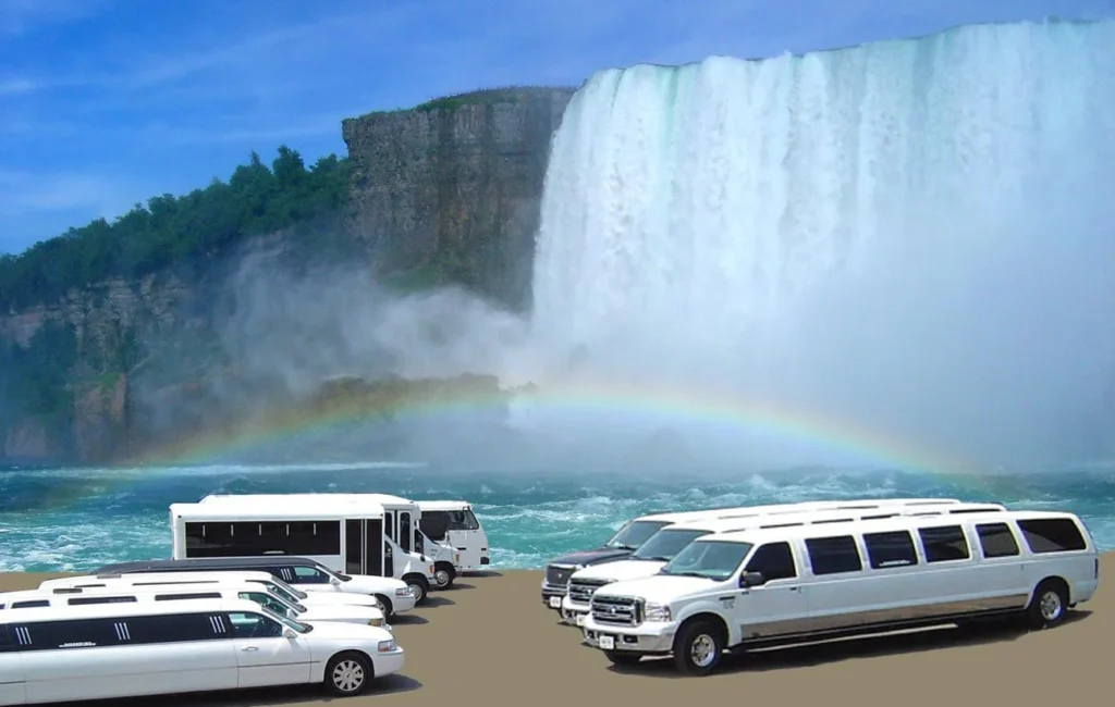 limo from toronto to niagara-White limousines and a bus parked near a powerful waterfall with mist and a vibrant rainbow. The scene conveys grandeur and natural beauty.