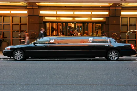 hidden costs taxis and rideshares-A sleek black limousine is parked on a city street, with a hotel entrance in the background. The dim lighting creates a luxurious and elegant atmosphere.