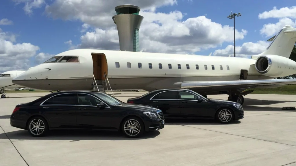 limo service orangeville-Private jet with open door on tarmac, flanked by two sleek black luxury cars. A control tower and scattered clouds are visible in the background.