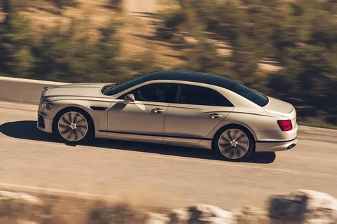 markham limo service-A sleek silver luxury sedan speeds along a sunlit, winding road. The car's polished finish glimmers, surrounded by blurred greenery, conveying motion.