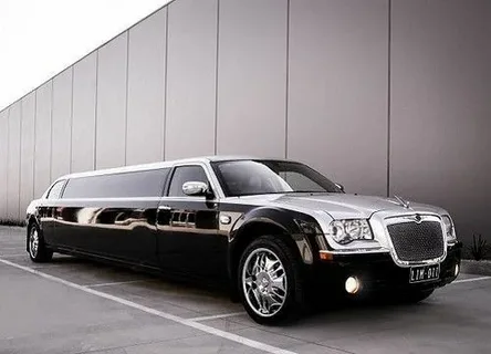 limo service milton-A sleek black and silver limousine parked by a modern building, reflecting sophistication and luxury. The car's polished exterior gleams in daylight.