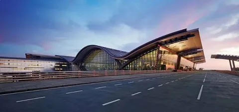 kingston limo service-A modern airport terminal with a wavy, futuristic roof design and large glass windows at dusk, under a vibrant, partly cloudy sky.