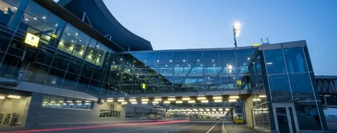 vaughan limo service-Modern airport terminal at dusk, featuring a vast glass facade with lit interiors and an enclosed walkway bridging two sections. A serene, twilight ambiance.