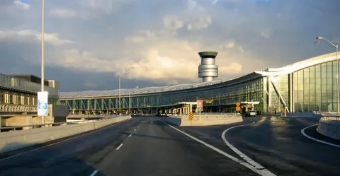 limo service milton-Curved airport terminal road with a glass facade and control tower against a cloudy sky. The scene is calm, with subdued lighting and no vehicles.