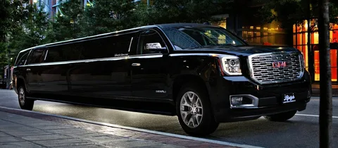 Mississauga Airport Limo Services -A sleek, black stretch SUV limousine is parked on a city street at dusk, with trees and illuminated shop windows in the background, exuding luxury.