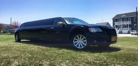 Brantford limo service-A sleek black limousine parked on a grassy area under a clear blue sky, with houses visible in the background, conveying luxury and elegance.