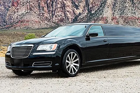 limo service milton-A sleek black limousine parked on a gravel surface, with a backdrop of rugged, multicolored rocky cliffs under a clear sky, conveying luxury and adventure.