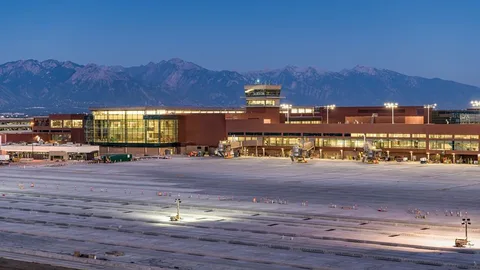 billy bishop airport limoEvening view of a modern airport terminal with large glass windows, illuminated under a clear sky. Snowy mountains form a scenic backdrop.-