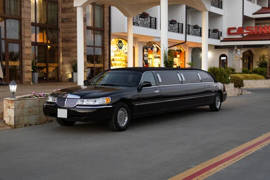 billy bishop airport limo-A sleek black limousine is parked in front of an elegant building with arched entryways and large windows. The scene suggests luxury and sophistication.