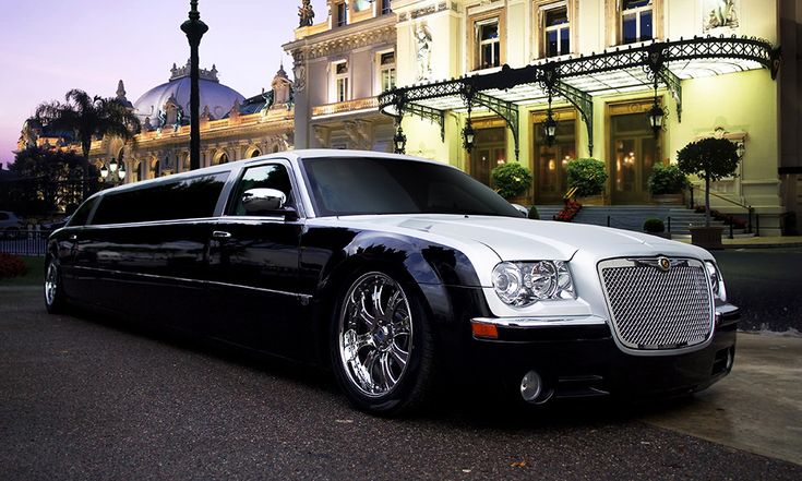 billy bishop airport limo-A sleek black and white limousine is parked on a street with a grand, illuminated building in the background. The scene conveys luxury and elegance at twilight.