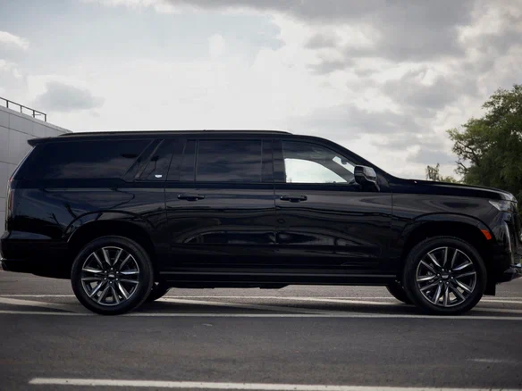 A sleek black SUV is parked on a road under a cloudy sky. The vehicle's shiny finish and tinted windows convey a sense of luxury and sophistication.