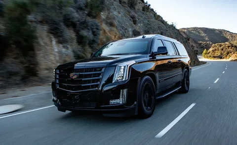 A sleek black SUV drives on a winding mountain road, surrounded by rocky terrain under a clear blue sky, conveying a sense of luxury and adventure.