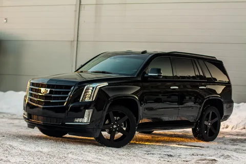 A sleek black SUV is parked on a snowy surface by a beige building. The vehicle's shiny finish and bold design convey luxury and power.