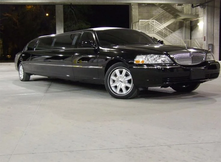 A sleek black limousine parked in a dimly lit garage, showcasing its shiny exterior and elegant design. The luxurious vehicle exudes sophistication.