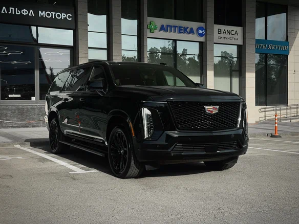 A sleek black SUV with a prominent front grille and distinctive vertical LED headlights is parked in front of a modern building with large windows.