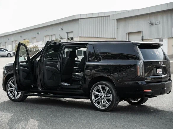 A black luxury SUV with all doors open is parked on a street. The setting is an industrial area with large warehouses, conveying sophistication and modernity.