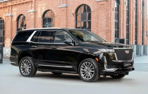 A sleek black SUV with shiny silver rims is parked in front of a historic brick building with tall, arched windows, conveying luxury and sophistication.