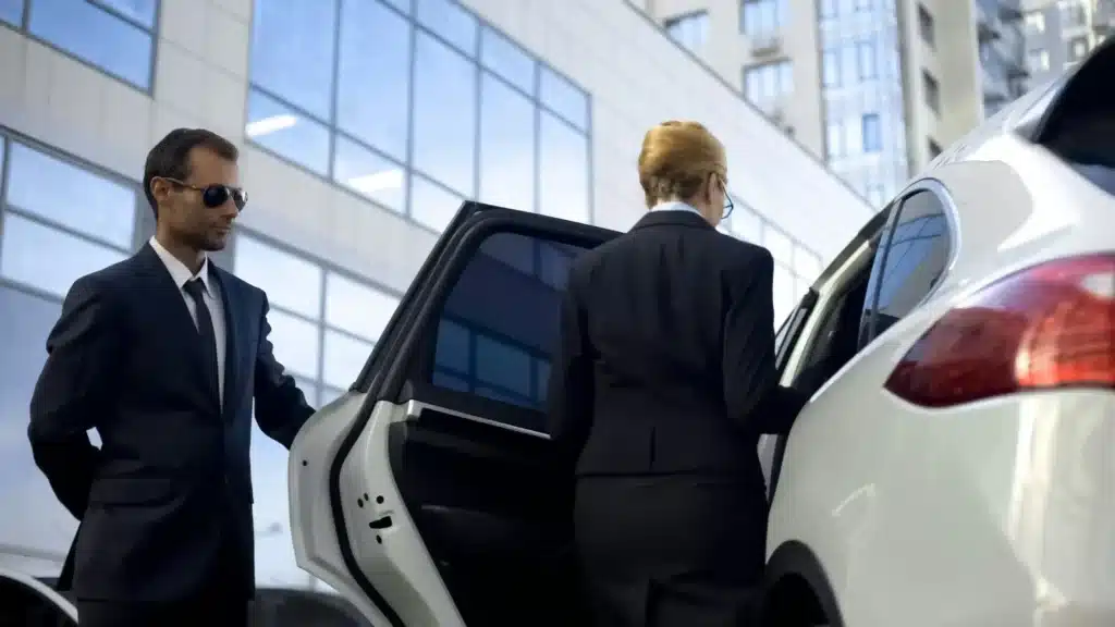 A chauffeur dressed in formal attire opening the door of a sleek black limousine to welcome a passenger.