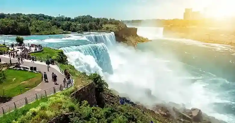 niagara falls limo service-Crowds admire the stunning Niagara Falls, with cascading water and lush greenery under a bright, sunny sky.