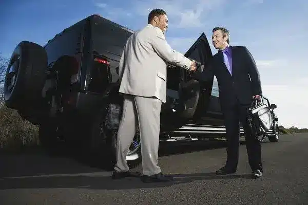 niagara falls limo service-Two men in suits shake hands on a road beside a large black SUV, suggesting a successful business meeting. The sky is clear, creating a professional and upbeat tone.